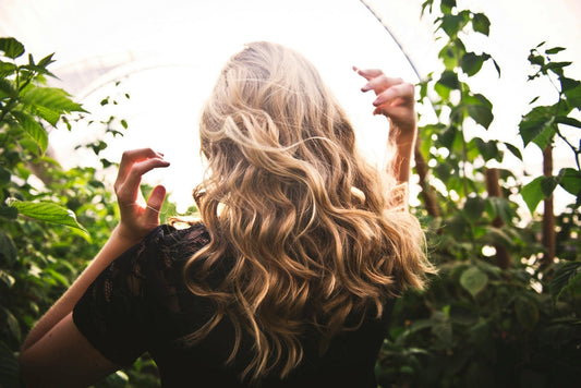 Woman in garden showing healthy wavy blonde hair illustrating vitamin-supported hair growth research