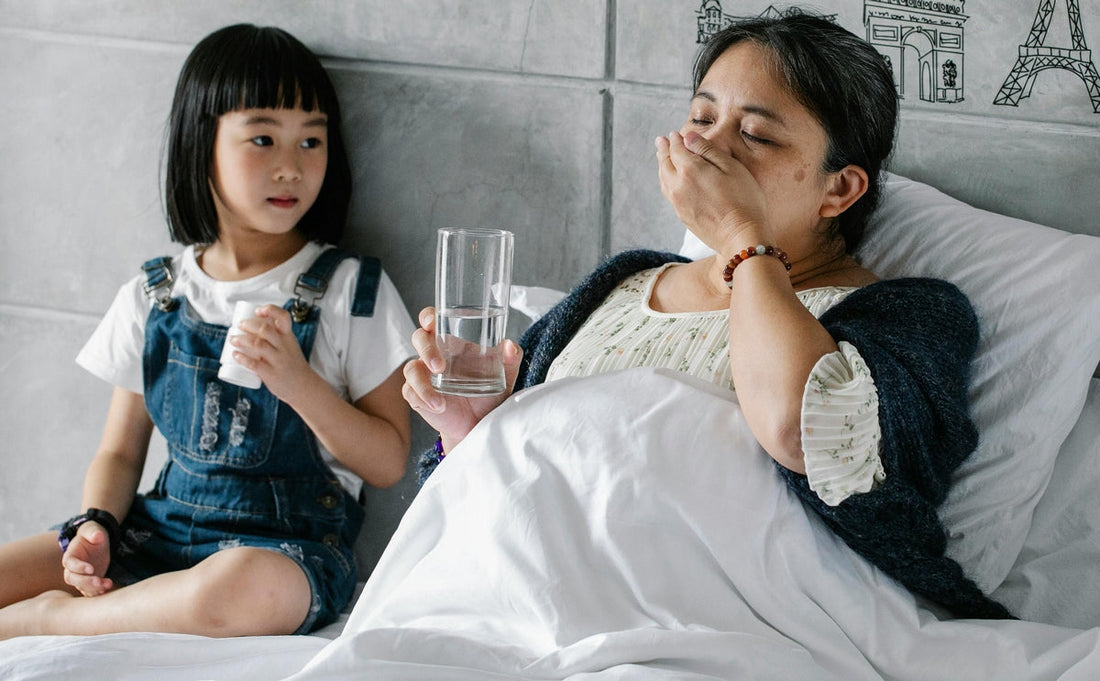 Mother recovering from illness taking biotin supplements in bed with her healthy daughter beside her