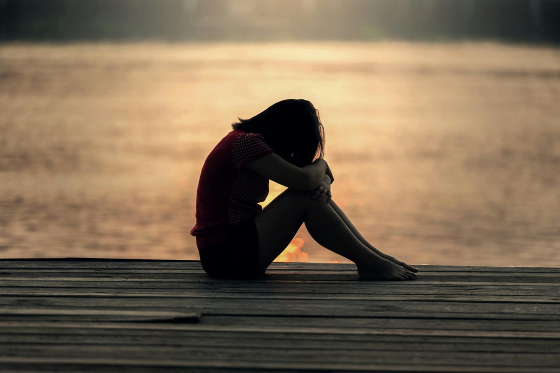 Woman sitting on dock by pond with head down, reflecting on anxiety relief through lysine