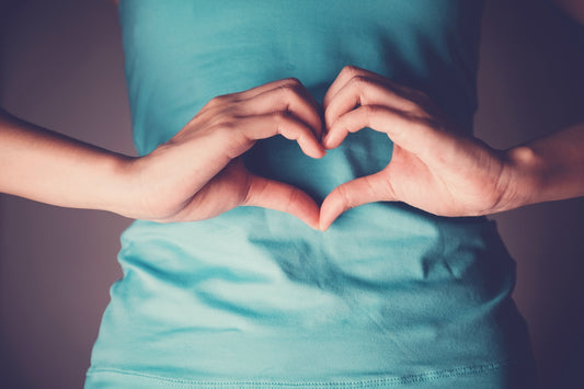 Woman making a heart shape with her hands over her stomach, symbolising gut health and balance between prebiotics and probiotics.