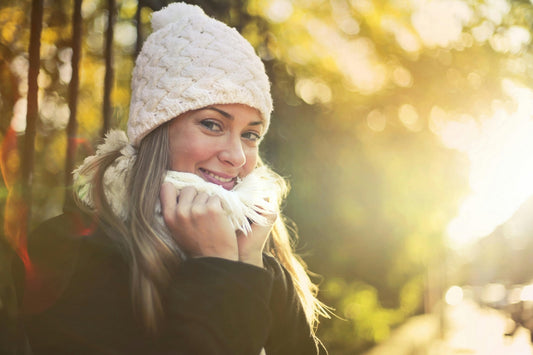 Smiling girl wrapped in a winter scarf and hat, enjoying the winter sun, highlighting the importance of vitamin D supplementation.