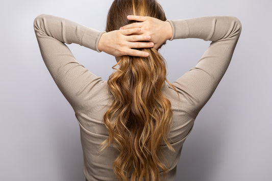 Woman with long, healthy hair tying it at the nape of her neck, showcasing the impact of vitamins on hair growth.